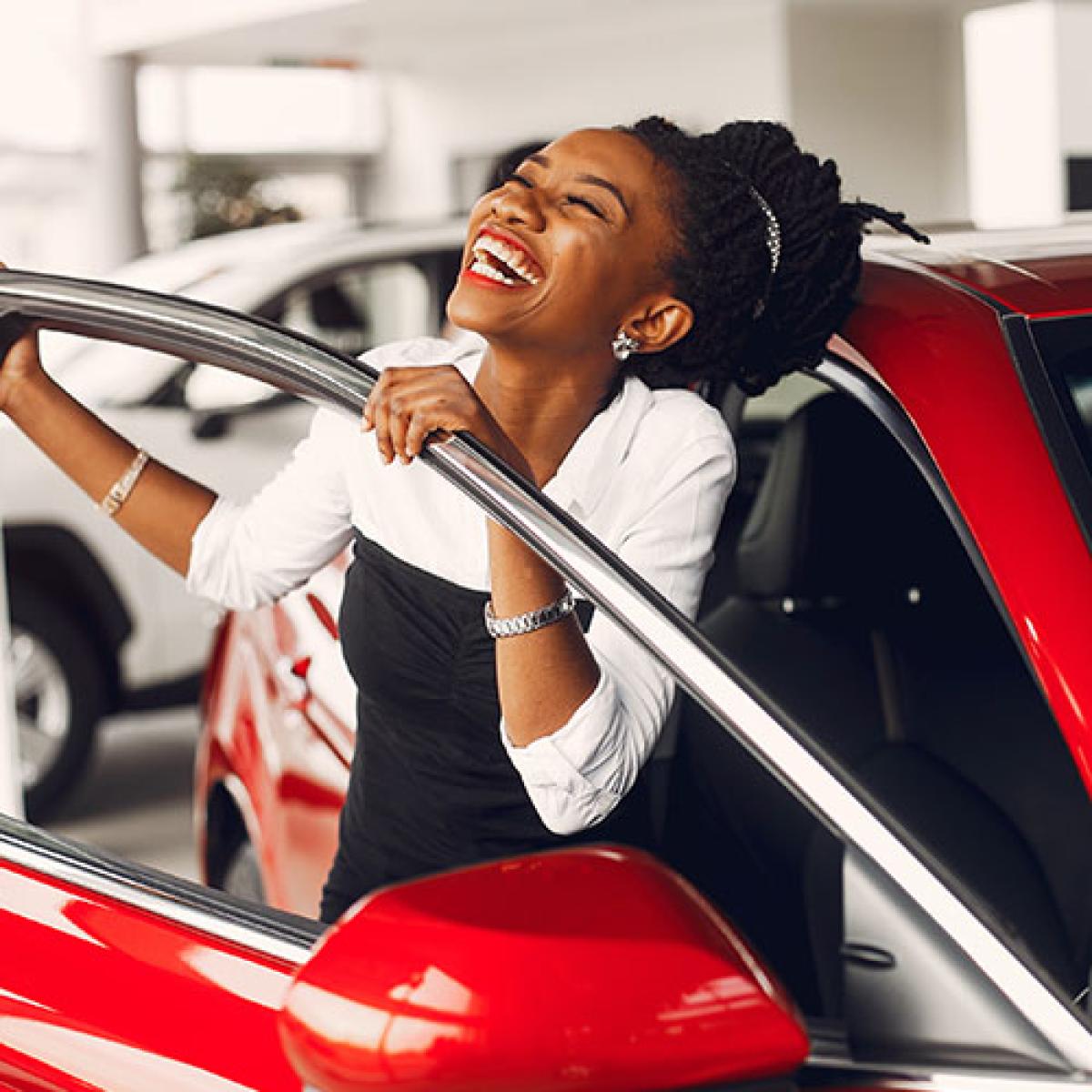 A woman smiling as she gets out of her red car.