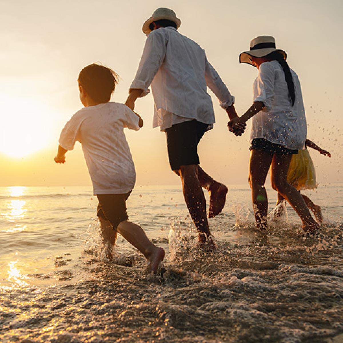 Family holding hands while running in the water at a beach.