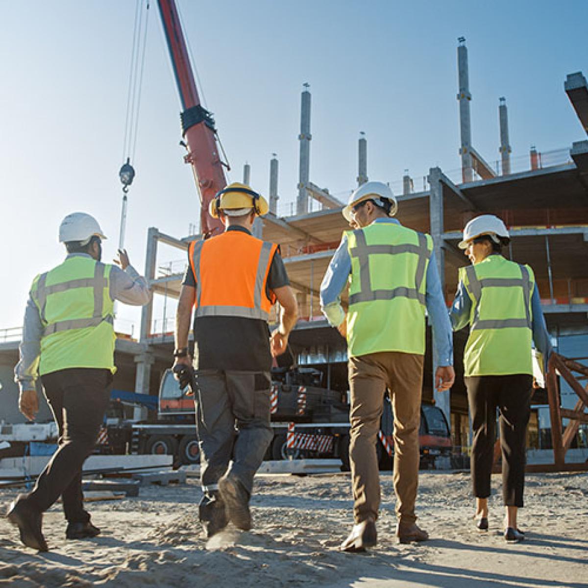 A group of men in high-visibility vests walks into a construction site.