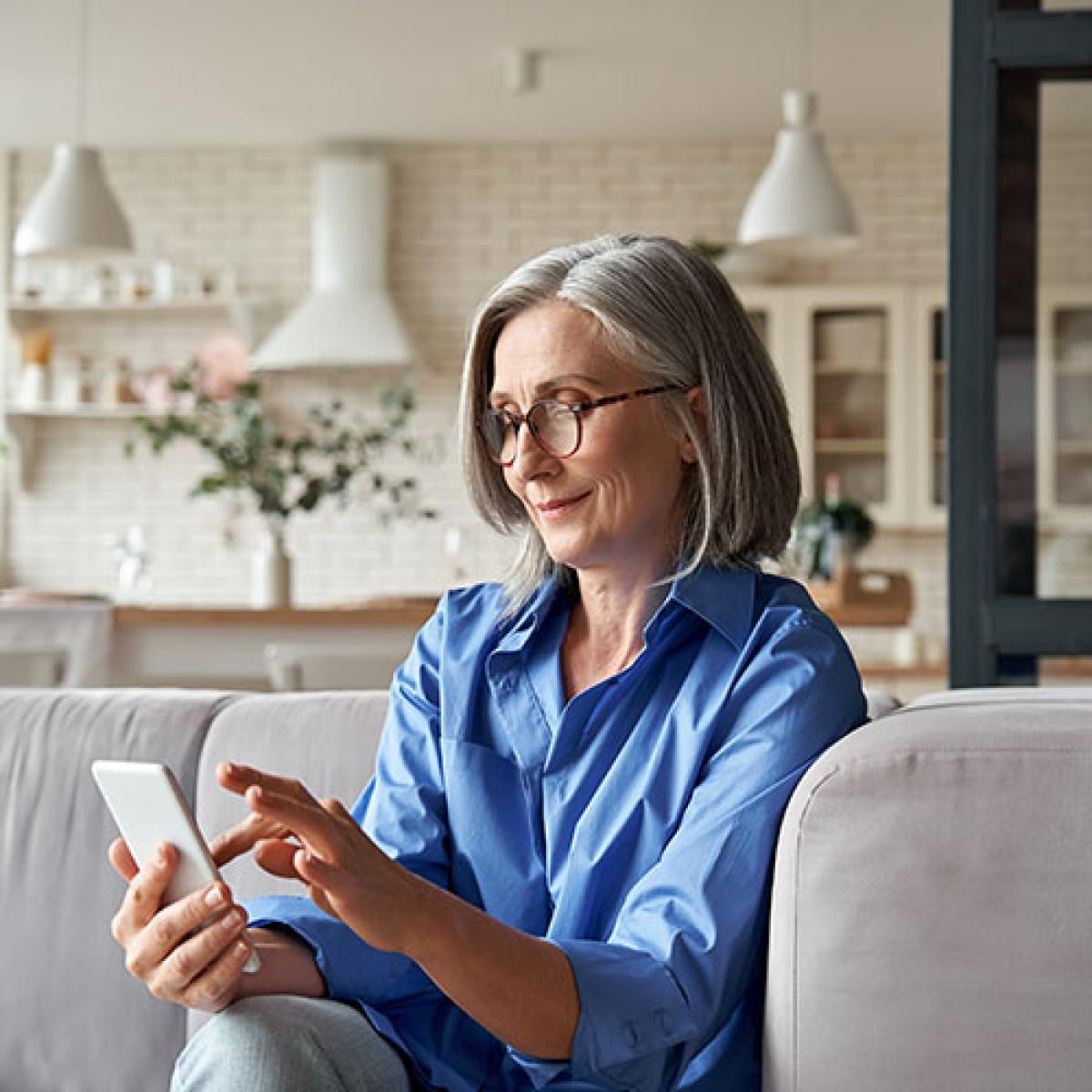 A woman sits on her couch looking at her phone.