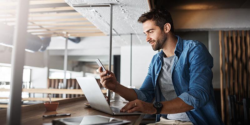 Man working on his laptop and looking at his phone.