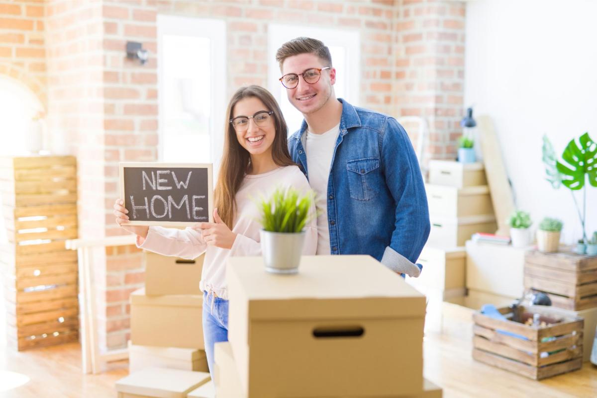 A couple holding boxes in their home and smiling at each other.