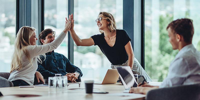 A woman high-fives another woman at a corporate meeting.