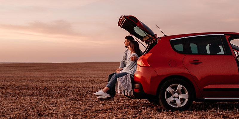 A couple sitting in the trunk of their car, looking out.