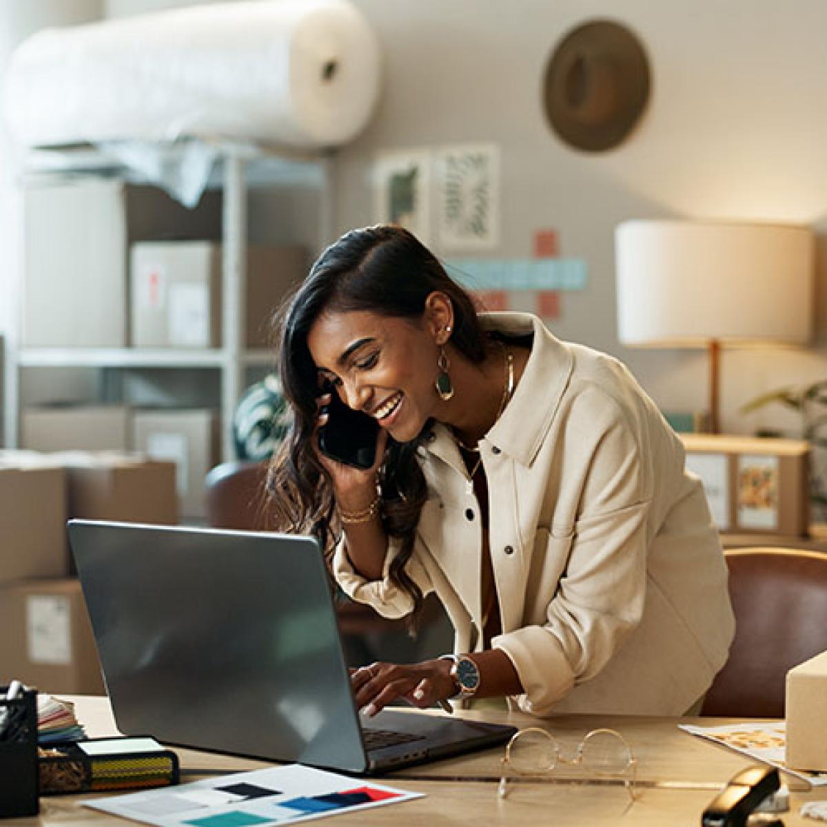 A smiling woman talking on the phone while typing on her laptop.