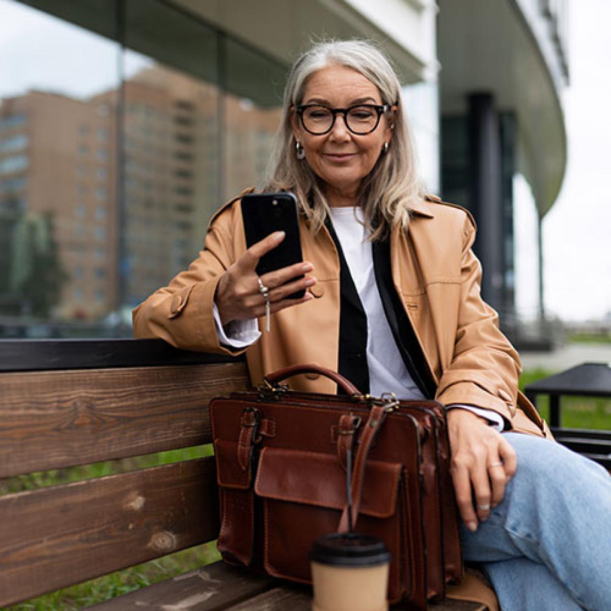 A woman sitting on a bench outside smiles as she looks at her phone.
