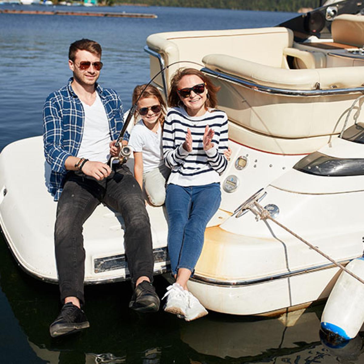A family sits on the edge of a pontoon boat fishing.