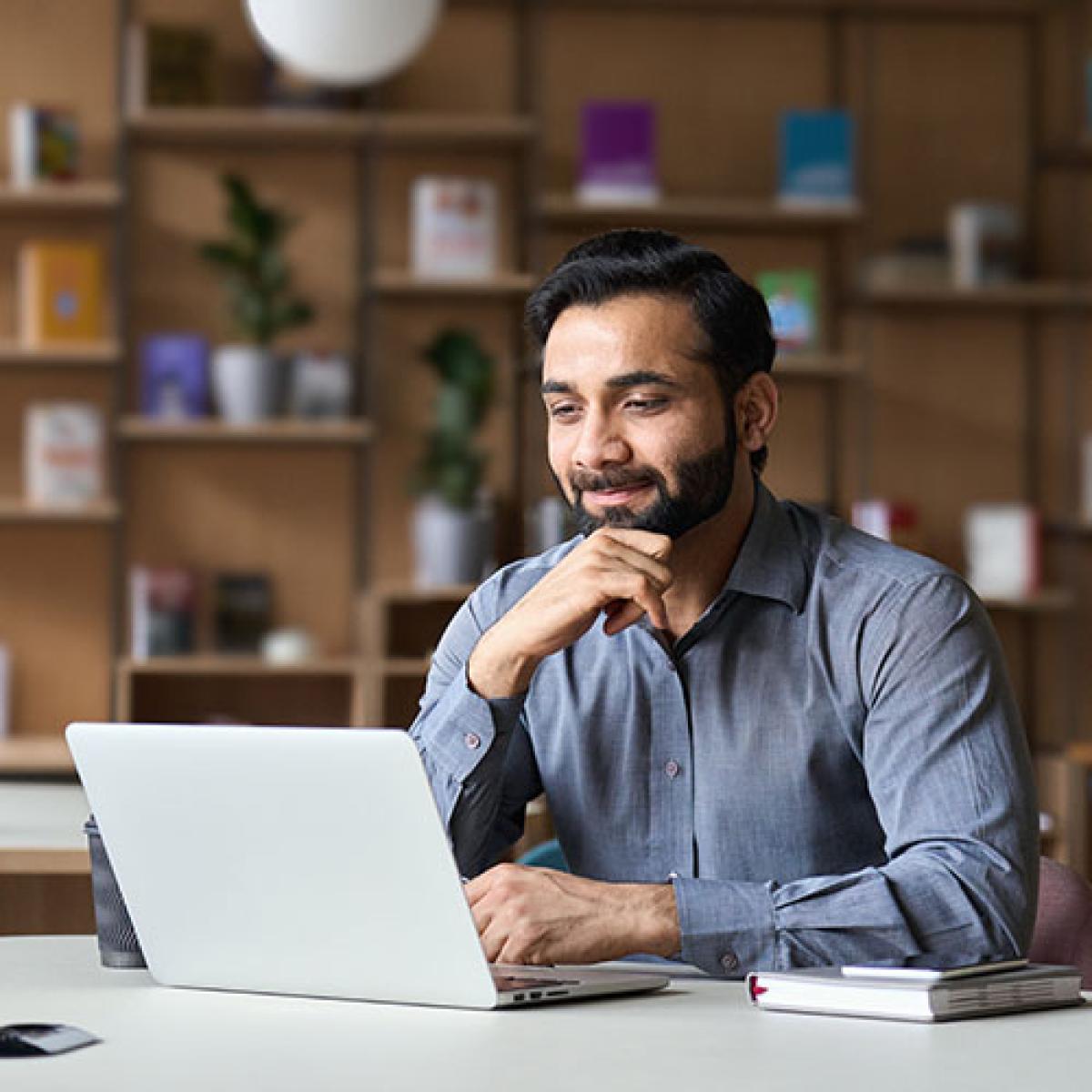 A man smiles as he looks at his laptop screen.
